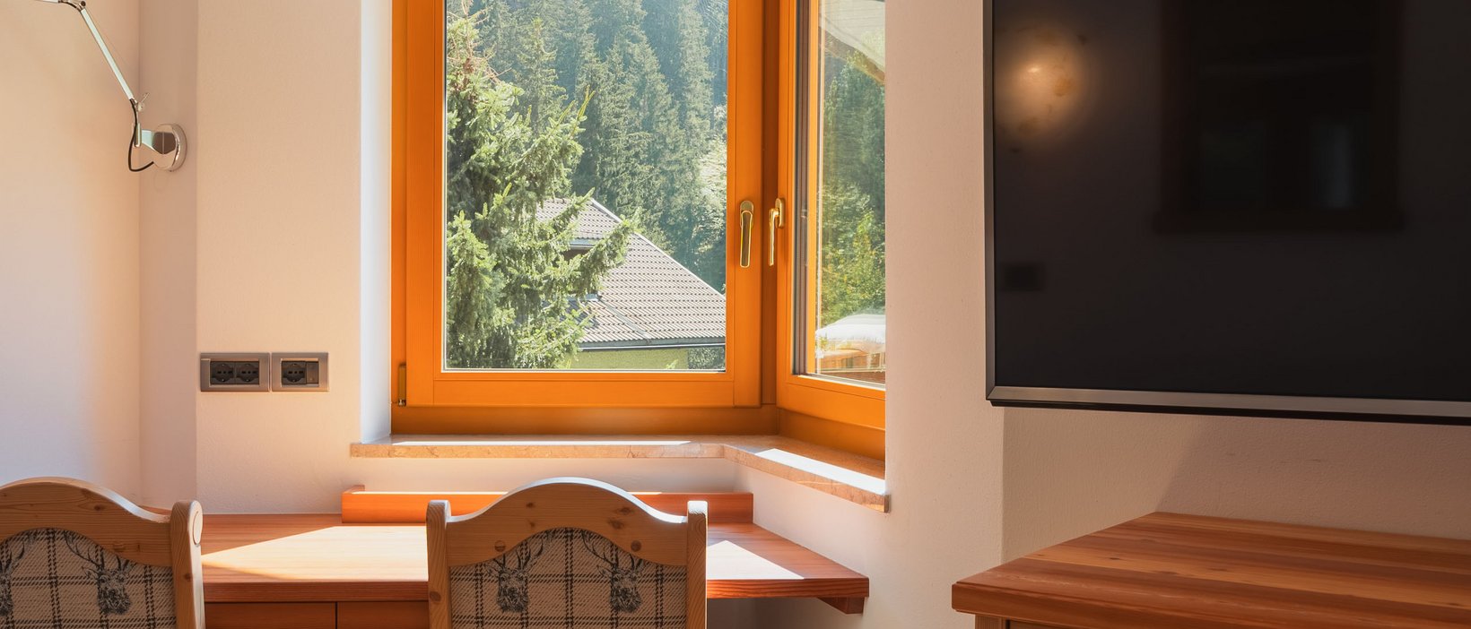 Reviews of our hotel in Val Pusteria/Pustertal with 4 stars Wooden desk with window view of green mountains and wall-mounted TV