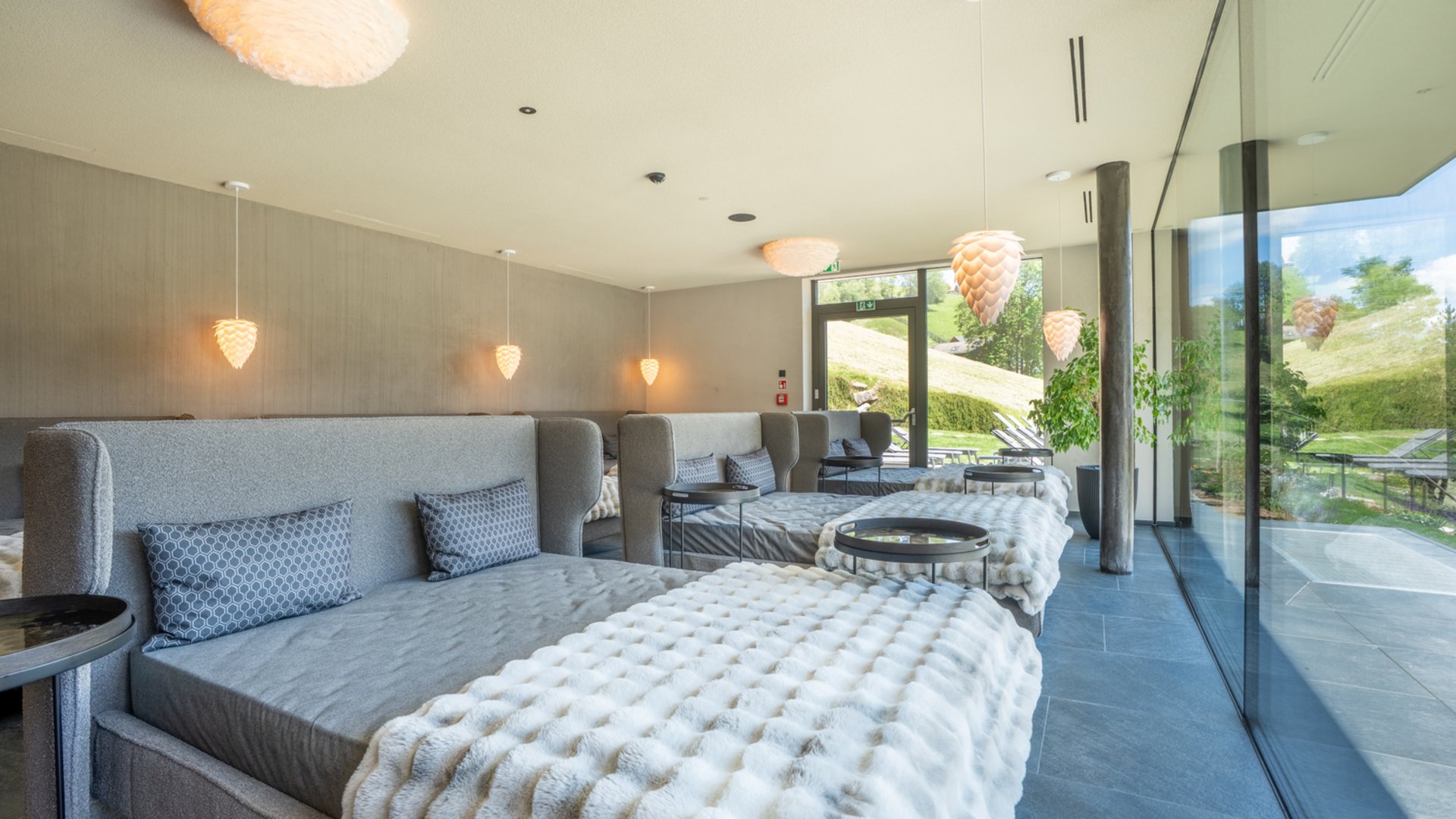Willkommen in Olang: Hotel Christoph Moderne Ruheliegen mit Decken und Kissen in einem hellen Wellnessraum mit Glaswand