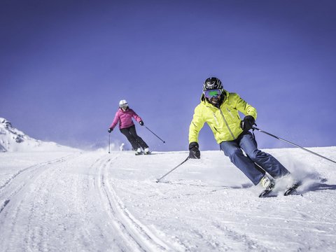 Leichte Wanderung am Kronplatz Zwei Skifahrer in bunter Kleidung fahren den schneebedeckten Hang hinunter