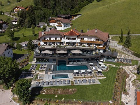 Sustainable 4-star hotel in the Dolomites Aerial view of a hotel with outdoor pool and sun loungers in green mountain landscape