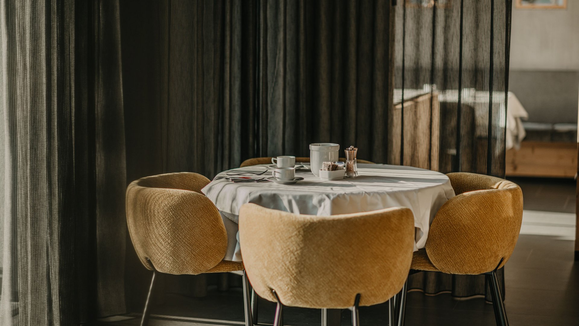 Willkommen in Olang: Hotel Christoph Runder Tisch mit weißer Tischdecke und vier braunen Stühlen vor dunklen Vorhängen