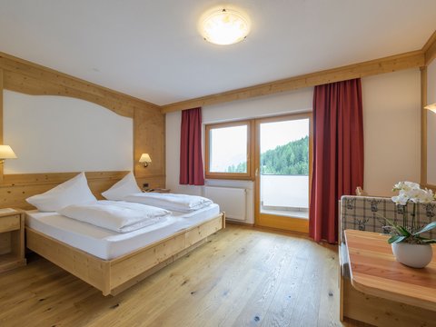Bewertungen unseres Hotels im Pustertal mit 4 Sternen Helles Schlafzimmer mit Doppelbett, Holzmöbeln und Blick auf Wald vom Balkon