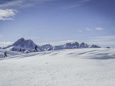 Your Plan de Corones/Kronplatz hotel on the slopes Three ski tourers hiking snowy hills with mountain range in the background