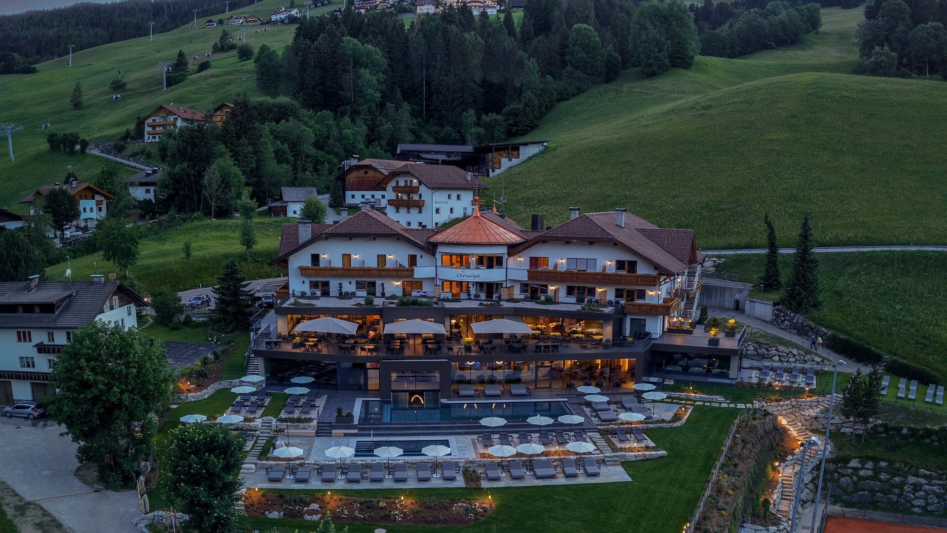 Willkommen in Olang: Hotel Christoph Hotel Christoph bei Abenddämmerung in grüner Berglandschaft mit Tennisplatz