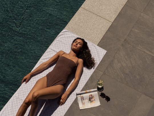 Willkommen in Olang: Hotel Christoph Frau im braunen Badeanzug entspannt auf Handtuch neben Pool mit Buch und Getränk