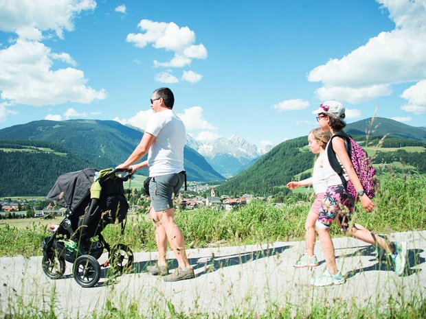 Sustainable 4-star hotel in the Dolomites Family walking with stroller on mountain path under sunny sky