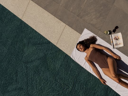 Willkommen in Olang: Hotel Christoph Frau liegt auf Handtuch neben Pool mit Buch, Getränk und Sonnenbrille