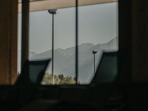 Fitness am Pragser Wildsee: Übernachtung im Hotel Christoph Bergblick durch großes Fenster in dunklem Innenraum mit Stühlen