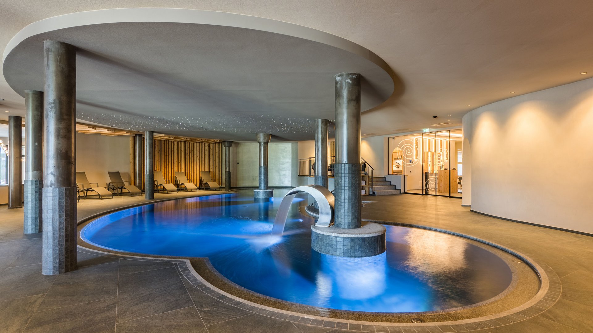 Willkommen in Olang: Hotel Christoph Innenpool mit Wasserfall und Liegestühlen in modernem Wellnessbereich