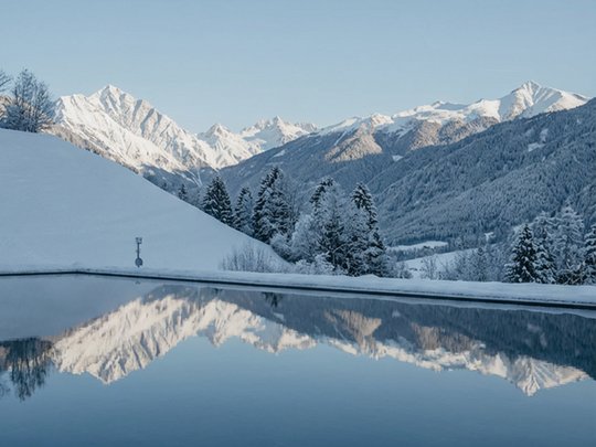 Willkommen in Olang: Hotel Christoph Schneebedeckte Berge spiegeln sich in einem ruhigen See unter blauem Himmel