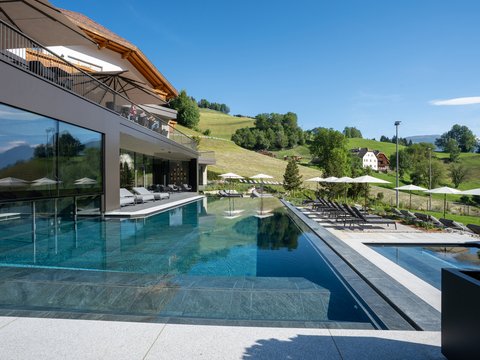 Willkommen in Olang: Hotel Christoph Moderner Außenpool mit Liegestühlen und Sonnenschirmen vor grünen Hügeln