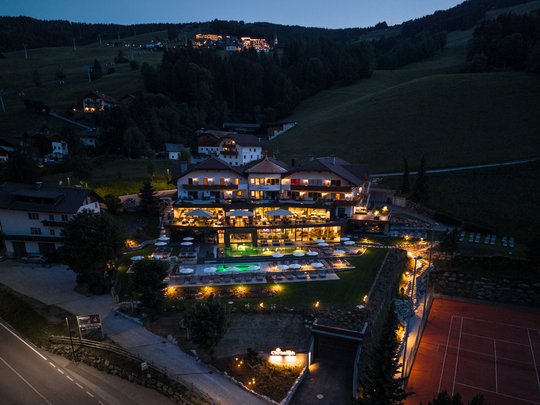 Willkommen in Olang: Hotel Christoph Beleuchtetes Hotel mit Pool und Tennisplatz in einer Berglandschaft bei Nacht