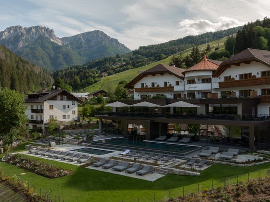 Willkommen in Olang: Hotel Christoph Hotel mit Außenpool und Liegestühlen vor Berglandschaft im Sommer
