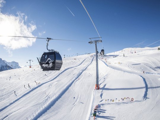 Your Plan de Corones/Kronplatz hotel on the slopes Ski lift and gondola on snowy mountain with skiers on a sunny day