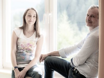 Standardzimmer Hotel Christoph Zwei Personen lächelnd vor einem großen Fenster mit Pflanzen