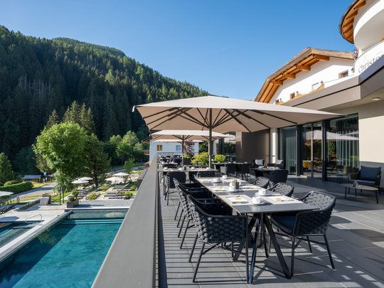 Willkommen in Olang: Hotel Christoph Terrasse mit Tischen, Stühlen und Sonnenschirmen neben Pool und Wald