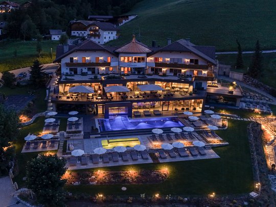 Willkommen in Olang: Hotel Christoph Beleuchtetes Hotel mit Pool und Liegestühlen in einer hügeligen Landschaft bei Nacht