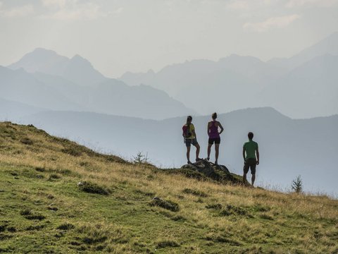 Your Plan de Corones/Kronplatz hotel on the slopes Three hikers standing on grassy hill looking at misty mountain landscape