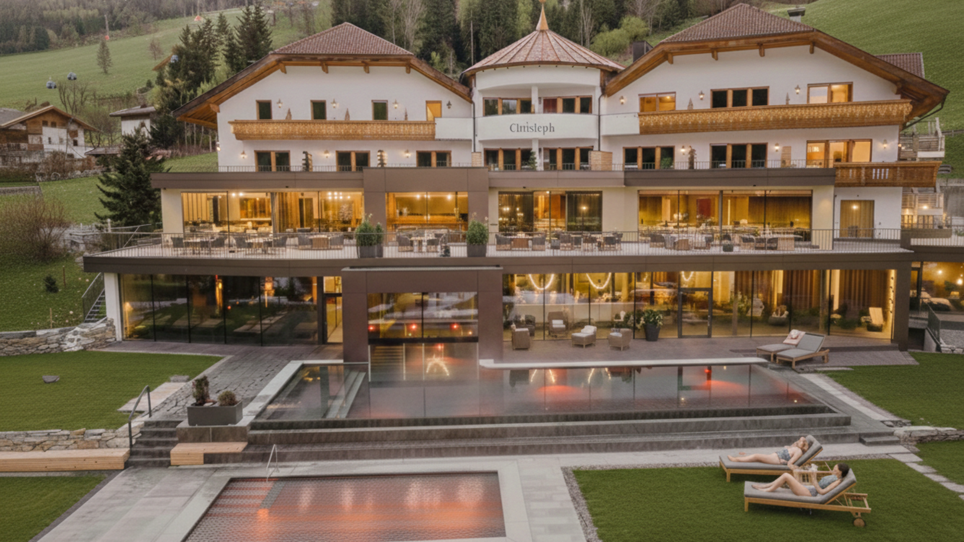 Willkommen in Olang: Hotel Christoph Luxushotel mit Pools und Liegestühlen vor Bergkulisse bei Abendlicht