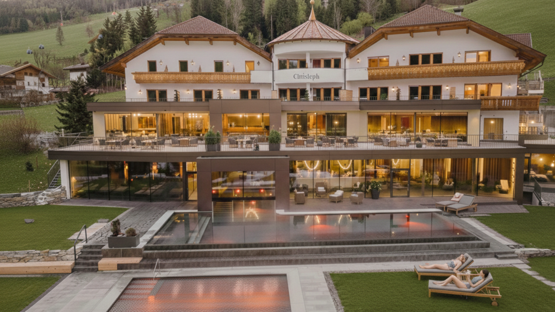 Willkommen in Olang: Hotel Christoph Luxushotel mit Pools und Liegestühlen vor Bergkulisse bei Abendlicht