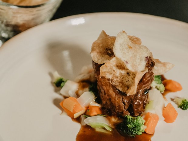 Sustainable 4-star hotel in the Dolomites Beef filet on vegetables with sauce and chips on a white plate